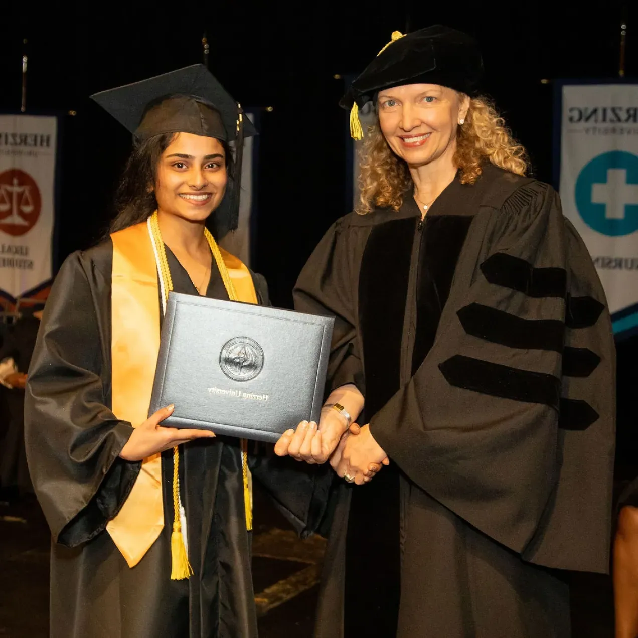 Herzing University graduation ceremony, professor shaking hands with a graduate holding their diploma.